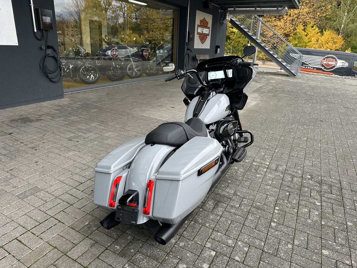 Harley-Davidson Touring Motorrad vor Händlerfiliale mit Werksfahrrad im Hintergrund.