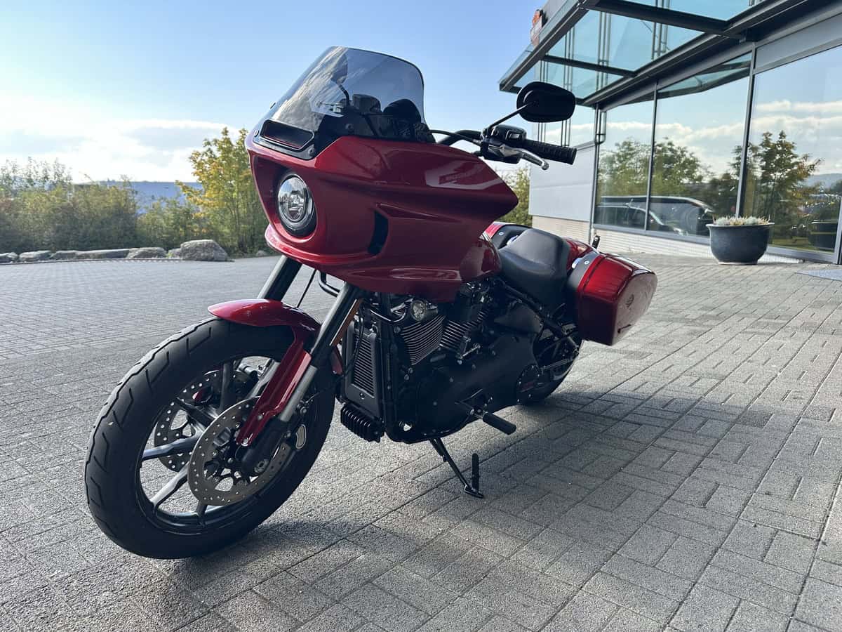 Harley-Davidson Motorrad mit rotem fairing und Windschild, vor einem modernen Gebäude.