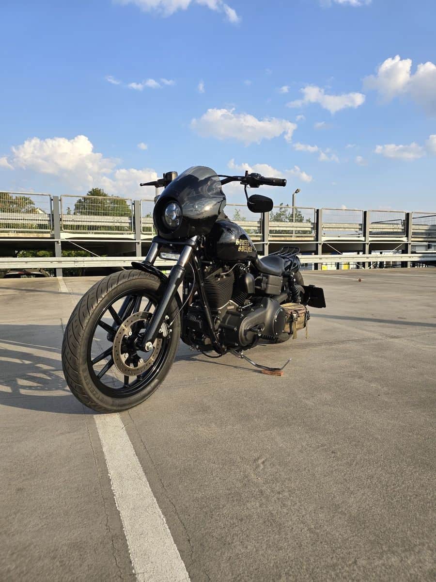 Schwarze Harley-Davidson Fat Bob auf Parkplatz bei schönem Wetter.