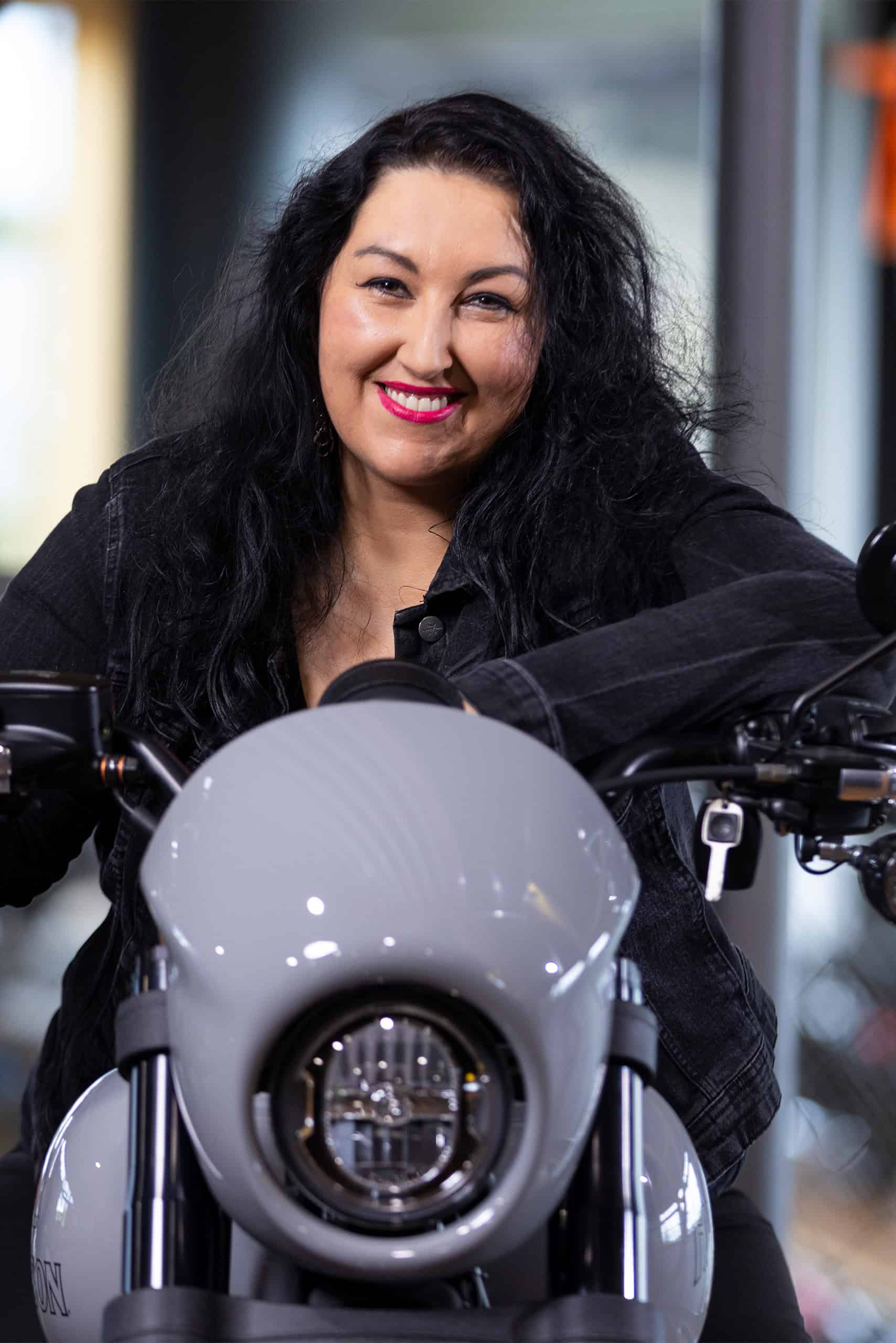 Frau mit schwarzen Haaren und rotem Lippenstift vor Harley-Davidson Motorrad.